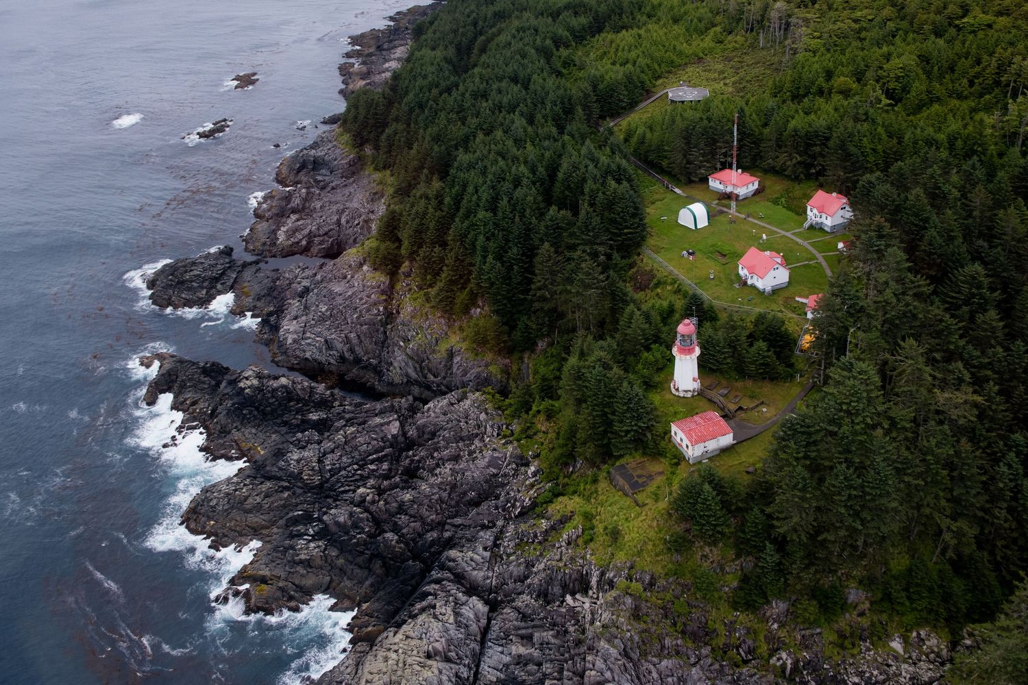 Aerial view of a rugged coastline with Langara lighthouse buildings and forest perched on rocky cliffs.