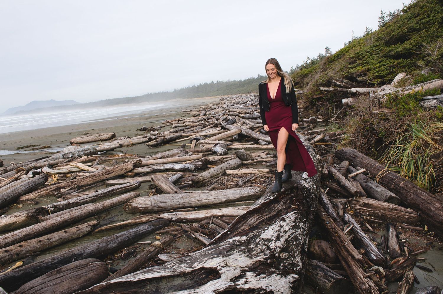 Dramatic coastal landscape with driftwood logs scattered along foggy beach.