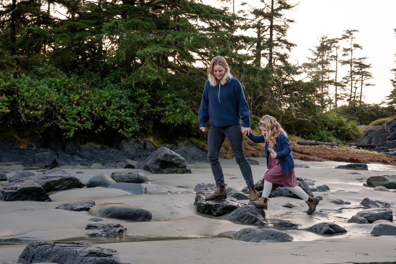 Group exploring a scenic beach with large rocks and pine trees along the Pacific Northwest coast.