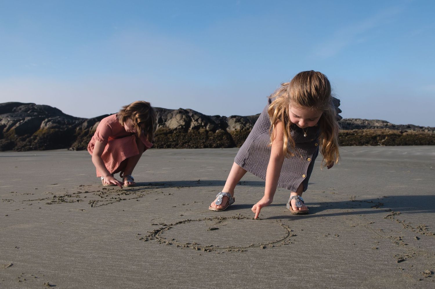 People crouching to draw in the sand on a serene beach at golden hour.
