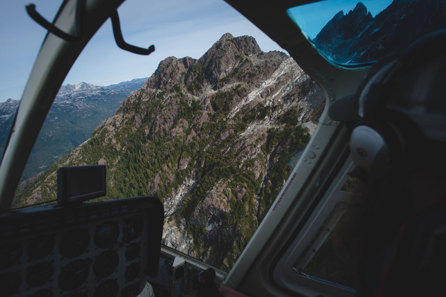Helicopter window view of dramatic mountain peaks and valleys below.