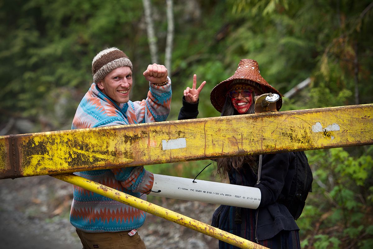 Fairy Creek blockade. Two protesters behind yellow barrier make peace signs while demonstrating.