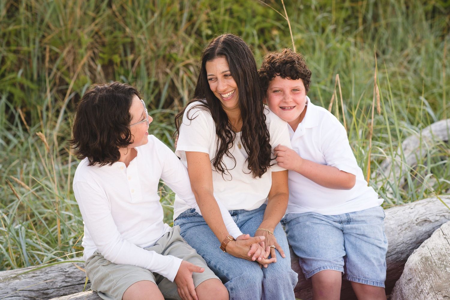 Relaxed family portrait session on beach with driftwood and natural coastal scenery.