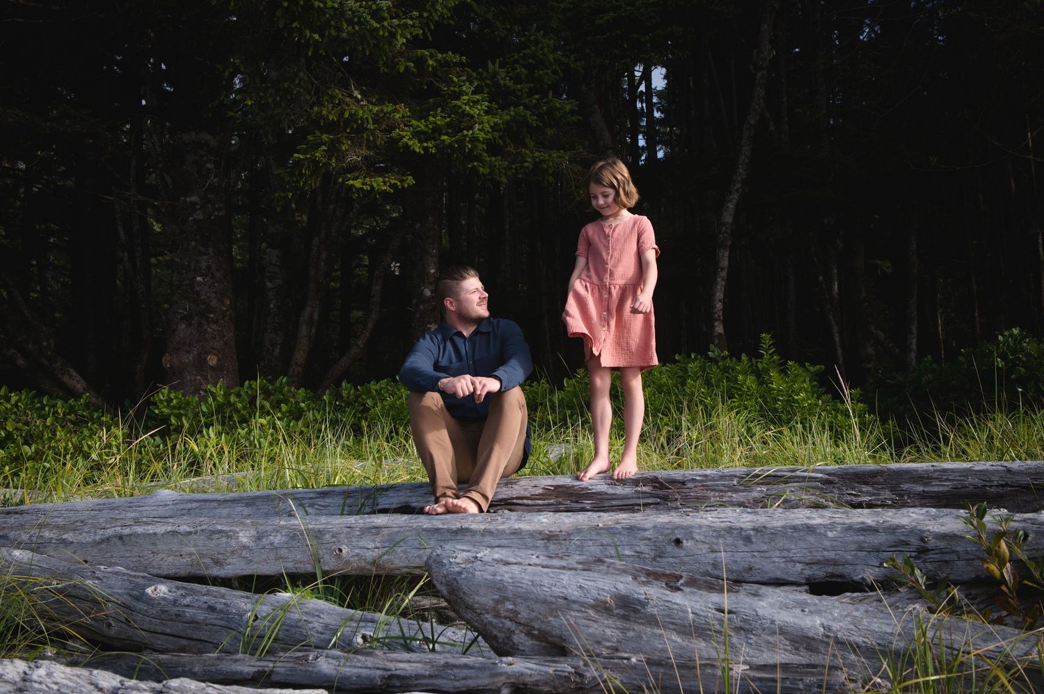 Two people explore a rocky beach landscape with trees in the background on a sunny day.