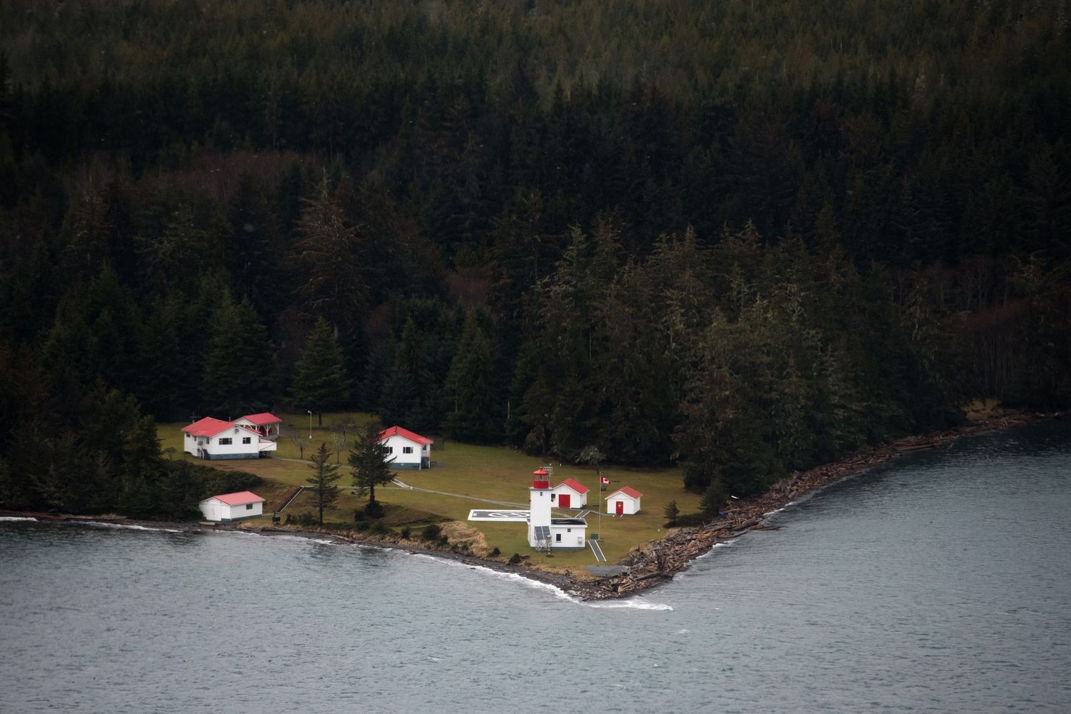 Scenic waterfront panorama with cabins nestled along a forested shoreline and mountains in the background.