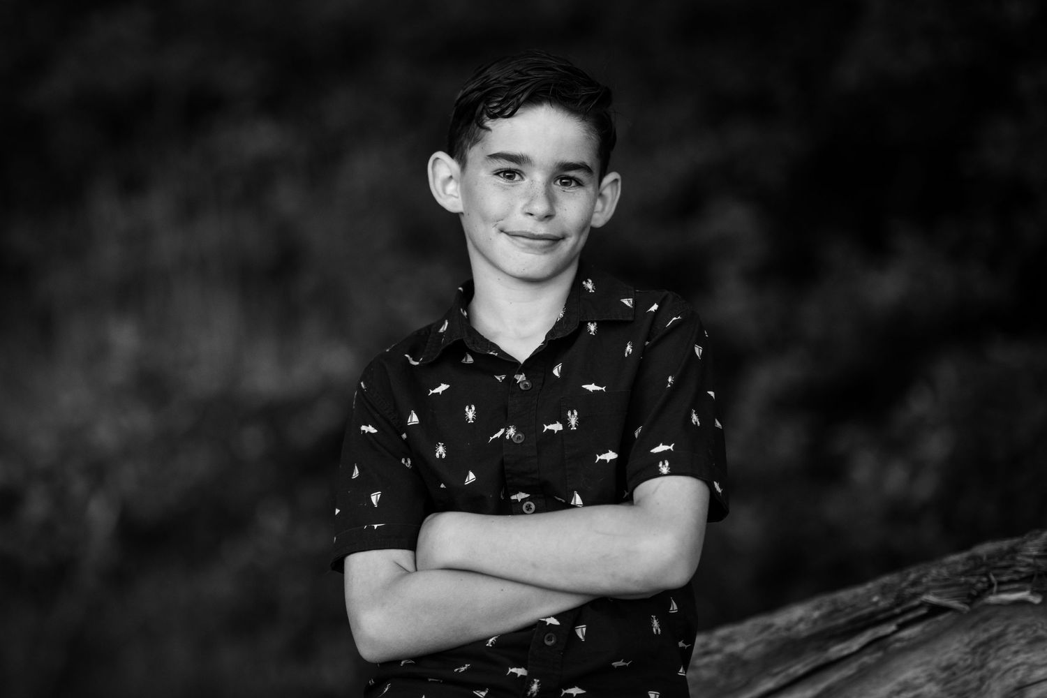 A young person in a polka dot shirt stands with crossed arms against a dark background.