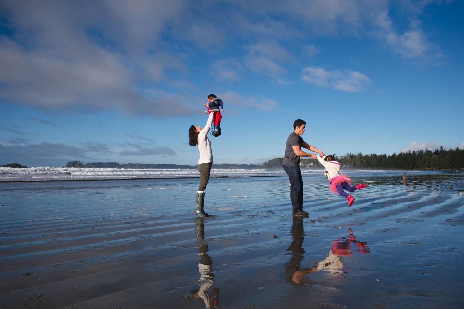 People walking along a vast beach shoreline under a bright blue sky with scattered clouds.