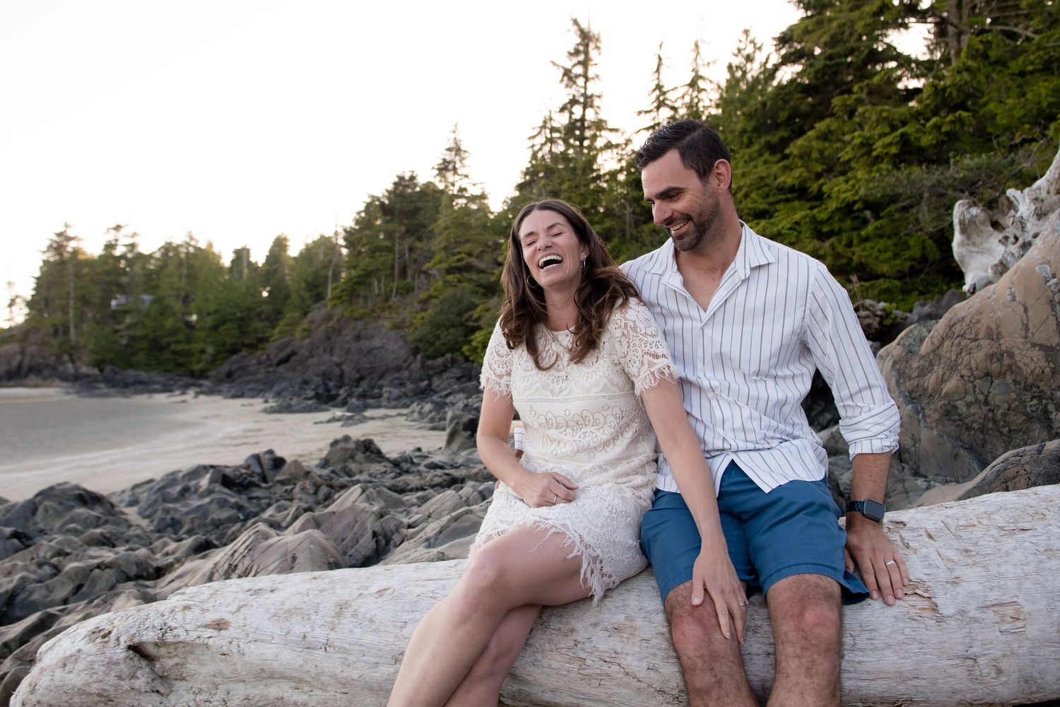 Couple sitting together on rocky beach during sunset along Pacific Northwest coastline.