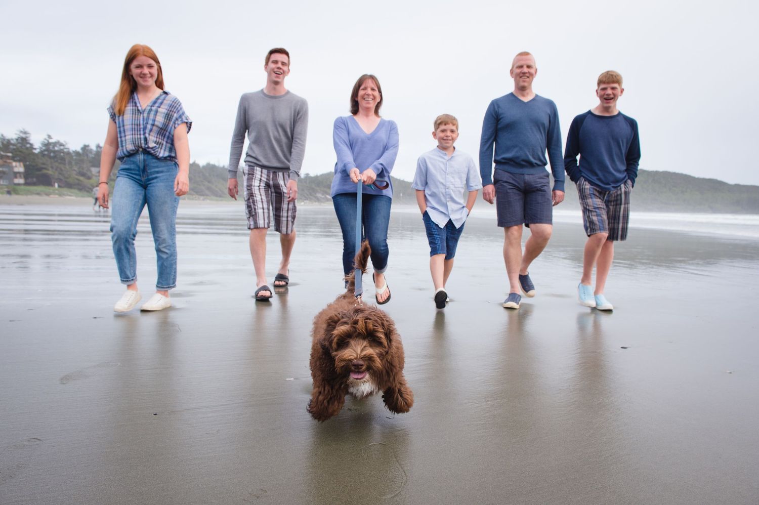 Family members standing together on sandy beach wearing coordinated blue and grey outfits.