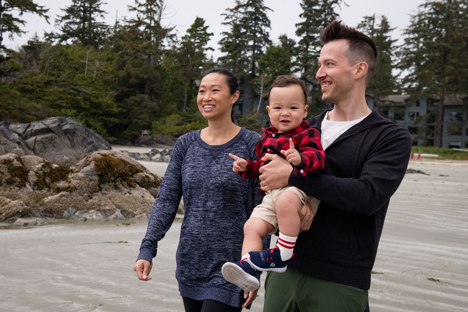 Family enjoying a casual stroll along a rocky beach with evergreen trees in the Pacific Northwest.