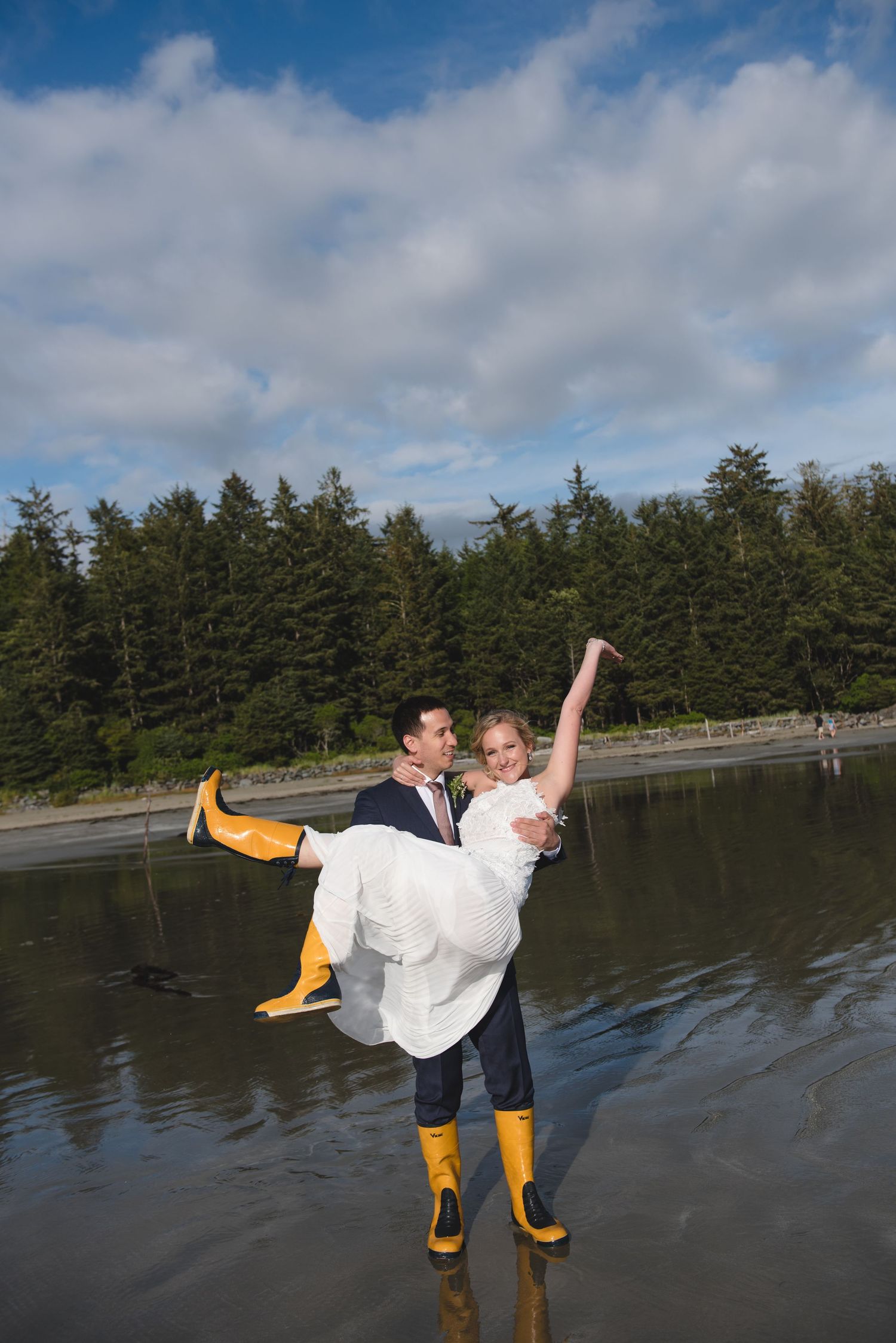A playful moment on a beach with yellow rain boots and formal wedding attire.