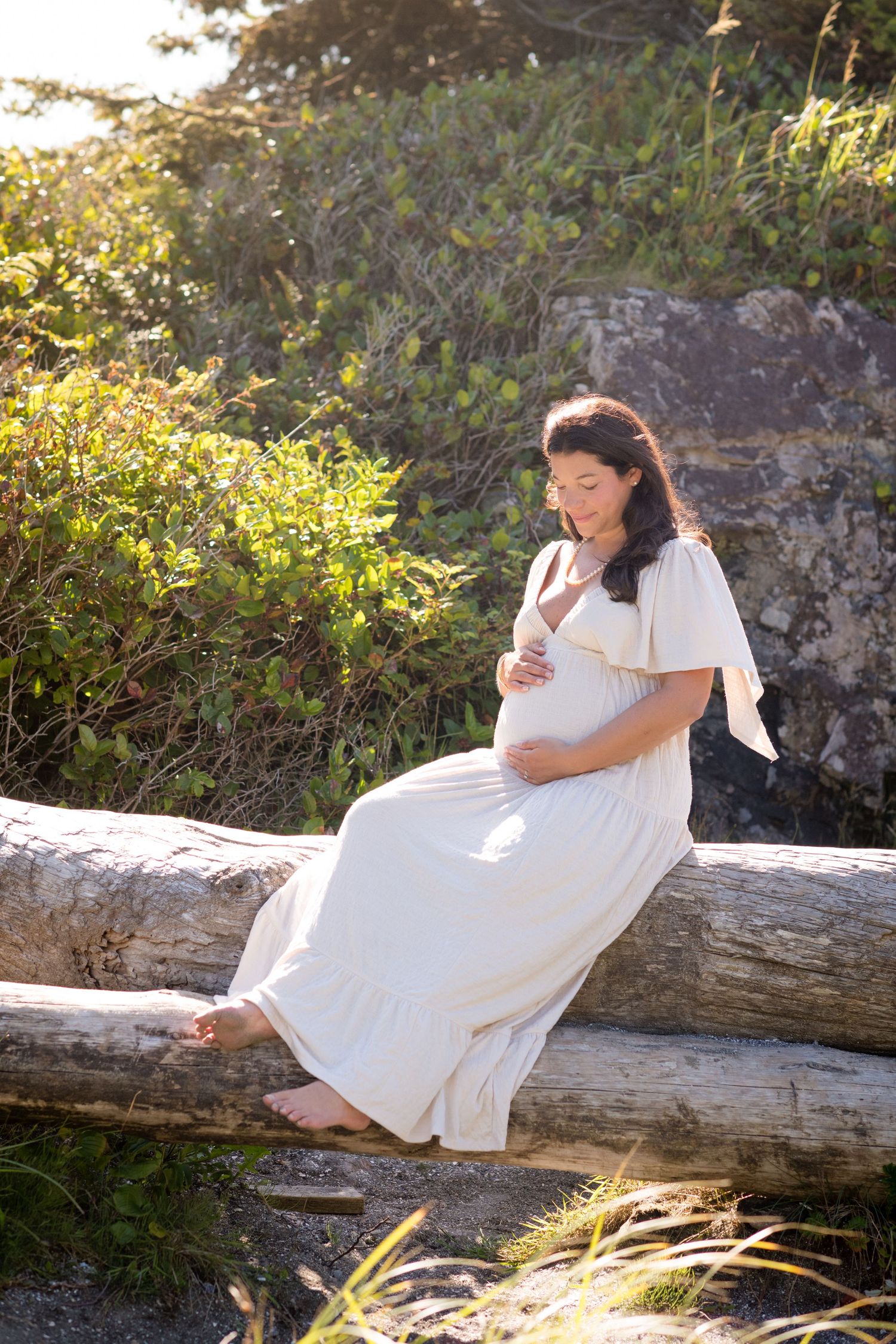 A couple shares an intimate moment while sitting on a fallen log surrounded by lush greenery.