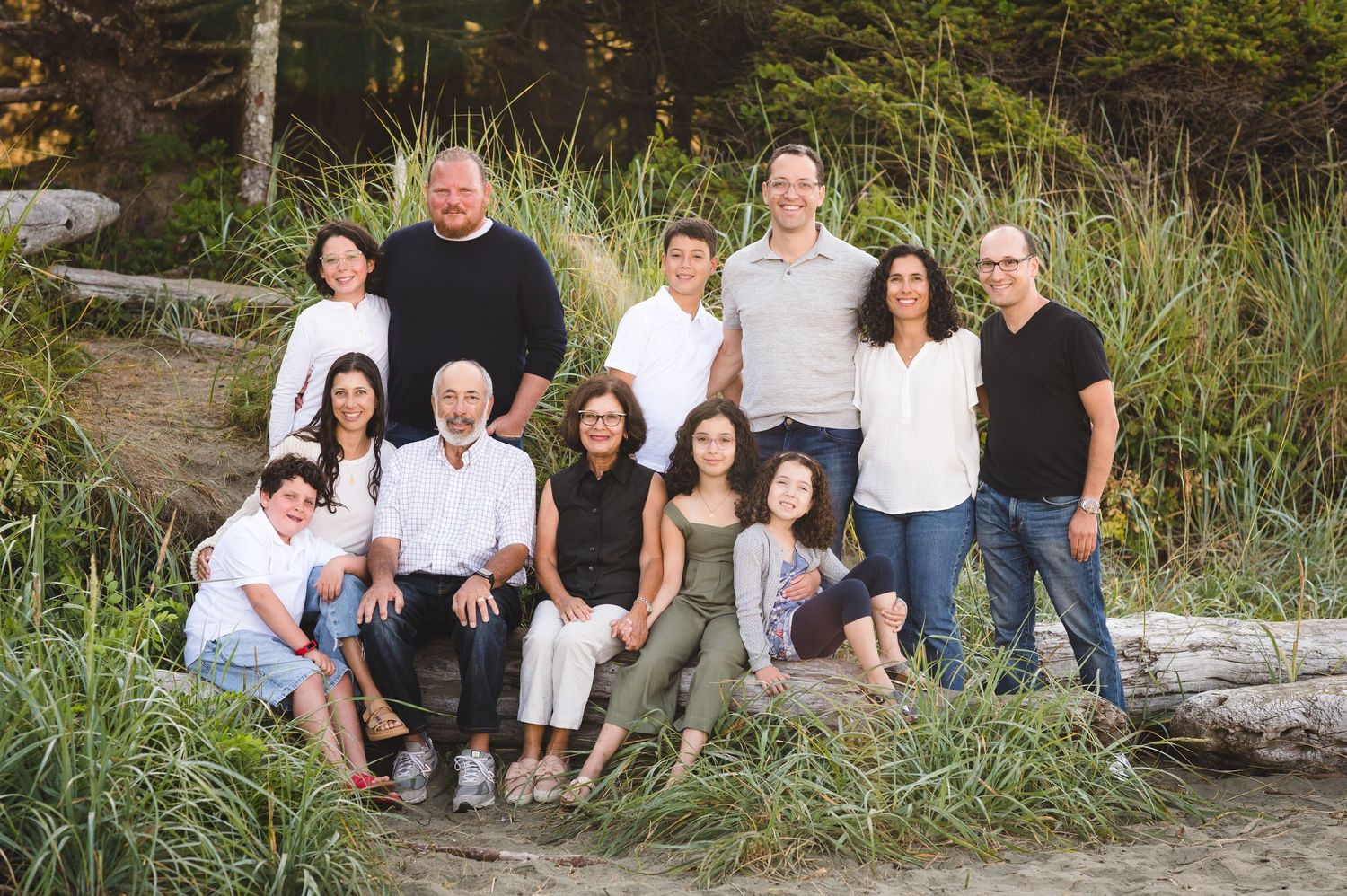 Group sitting together on driftwood at a beach surrounded by tall grass on a sunny day.