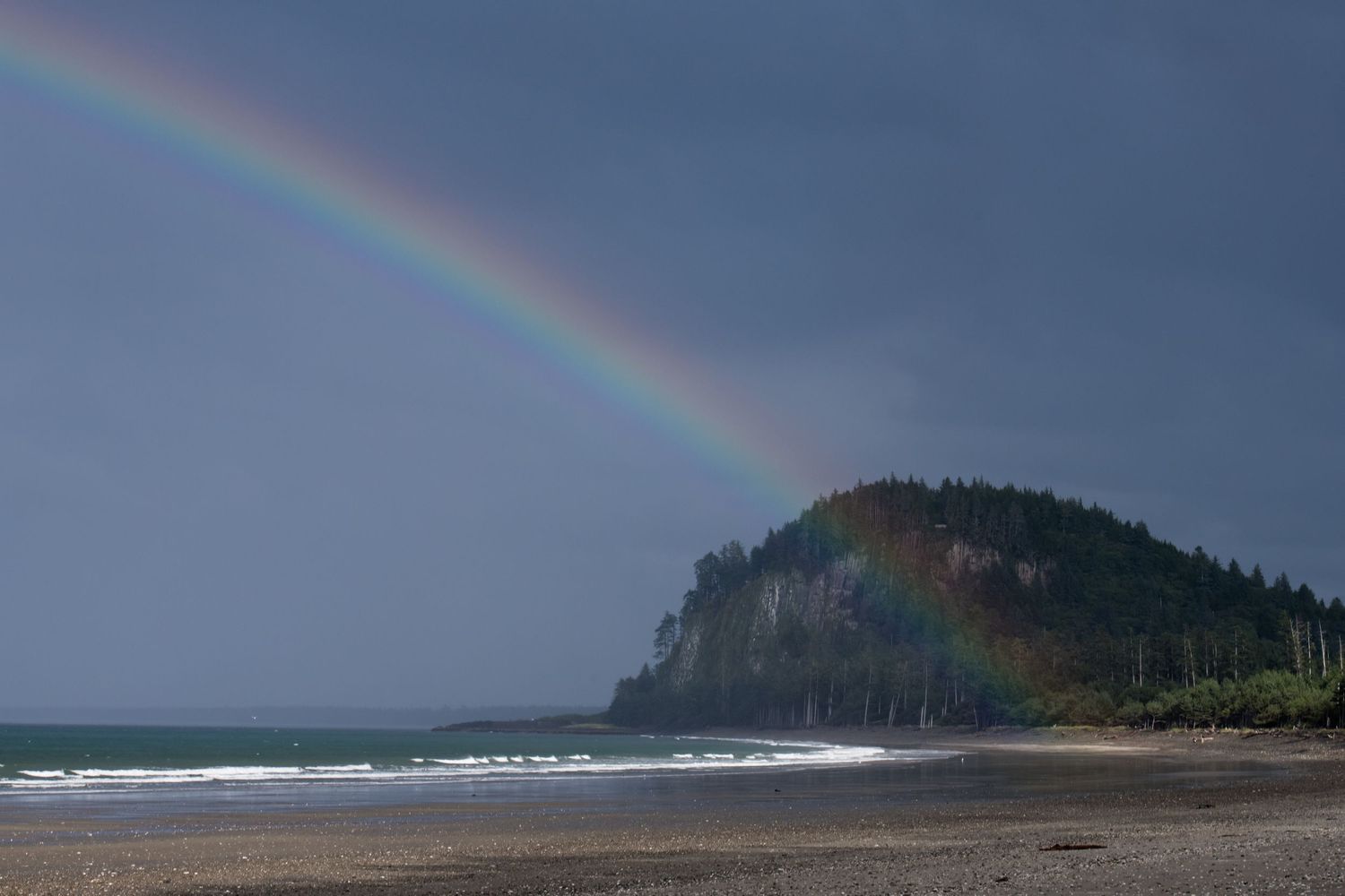 Vibrant rainbow arches over a dramatic coastal landscape with dark cliffs and crashing waves.