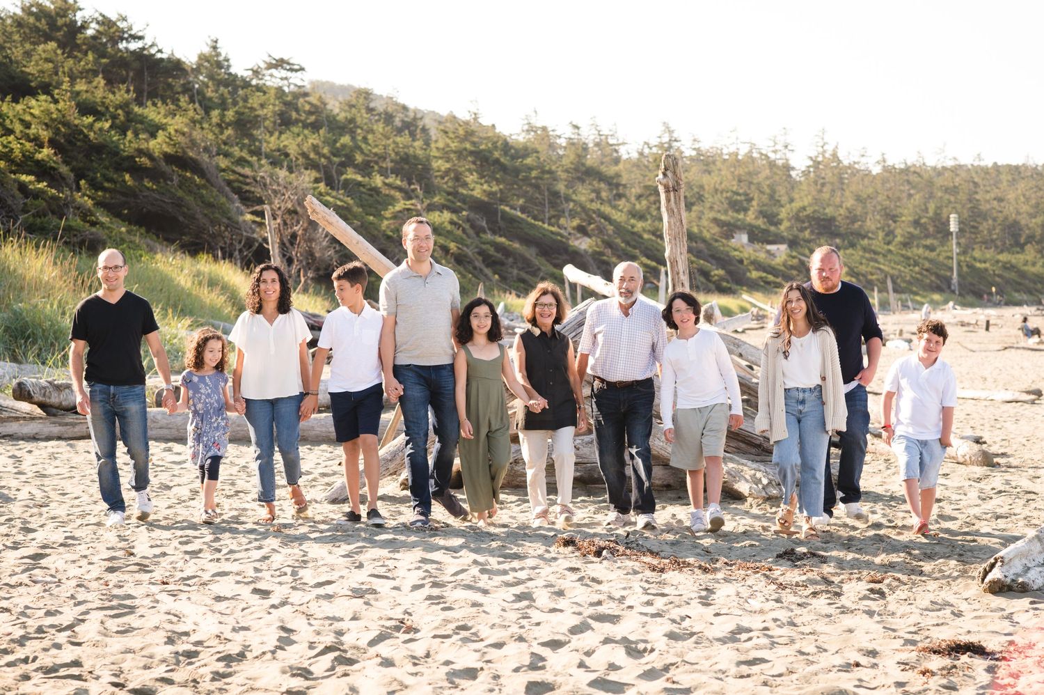A large family group poses together on a sunny beach with trees in the background.