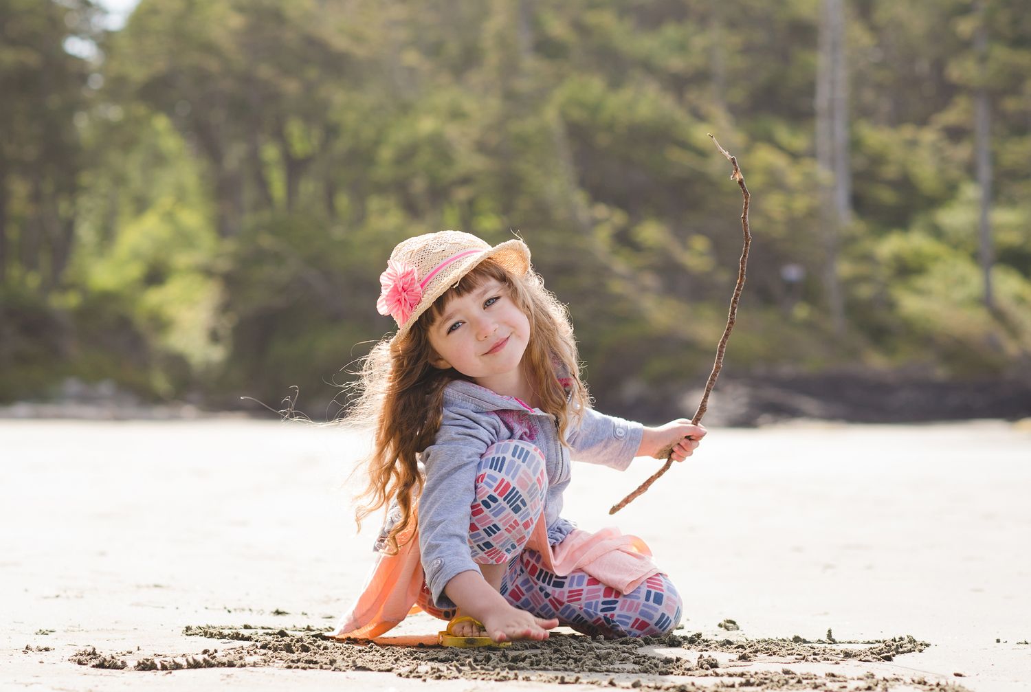 A person in a floral dress lies on a sandy beach while reading a book on a sunny day.
