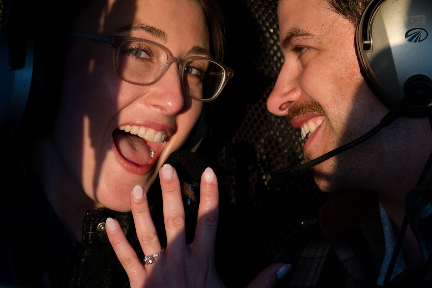 Couple celebrates helicopter proposal as woman shows off engagement ring while smiling joyfully in Tofino.