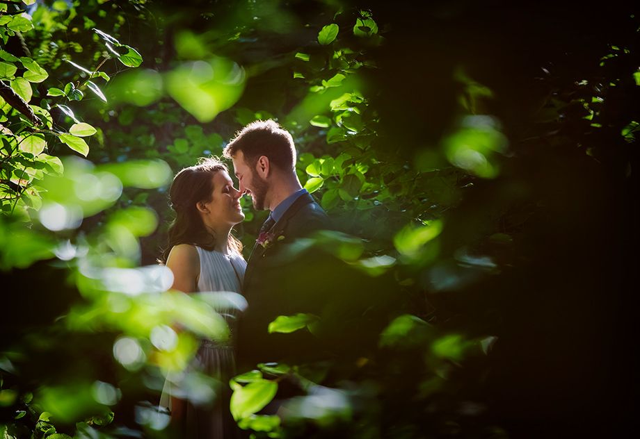 Wedding couple photographed through lush green forest foliage.