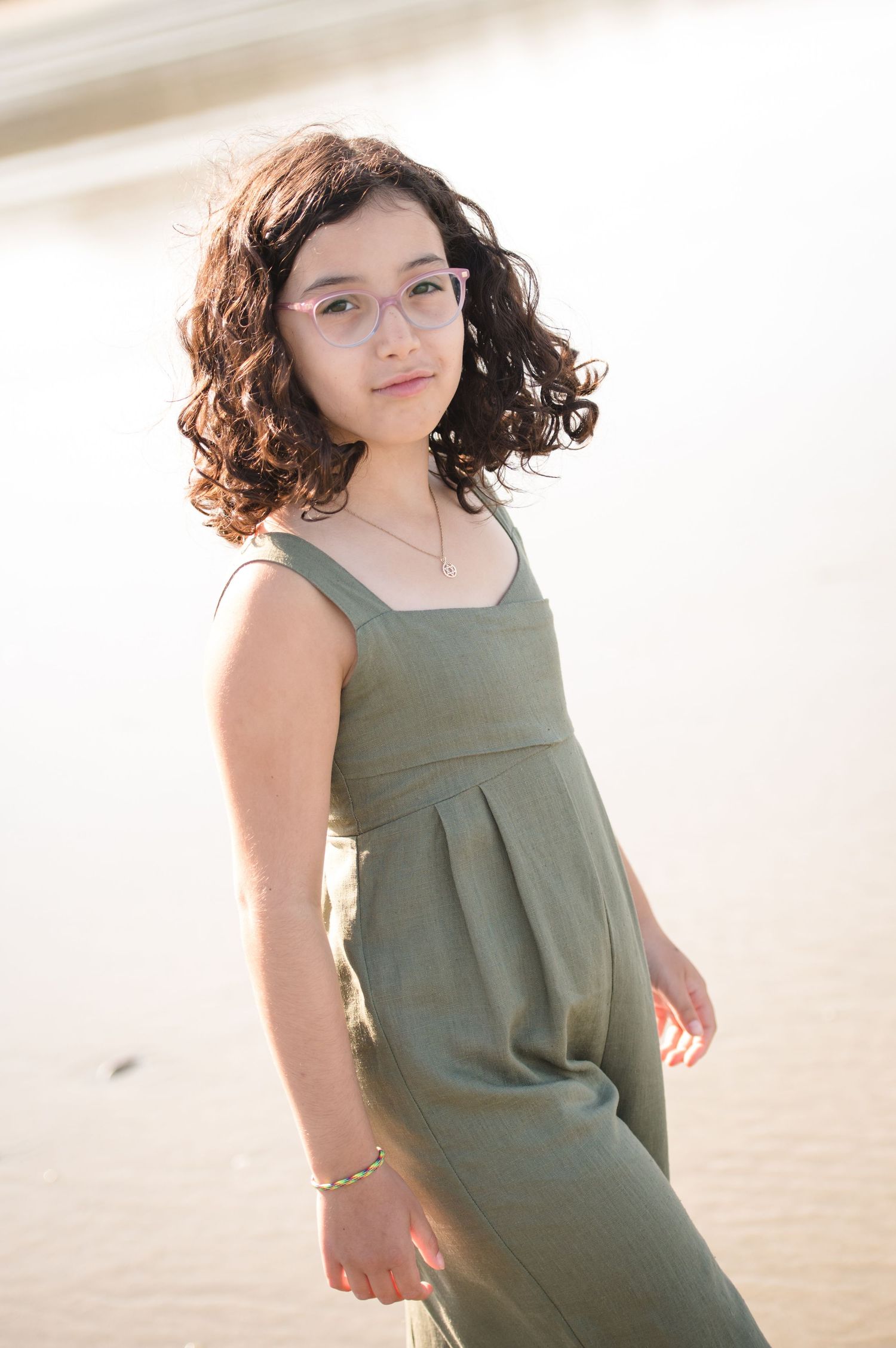 Young person in olive green dress posing on beach during golden hour photography session.