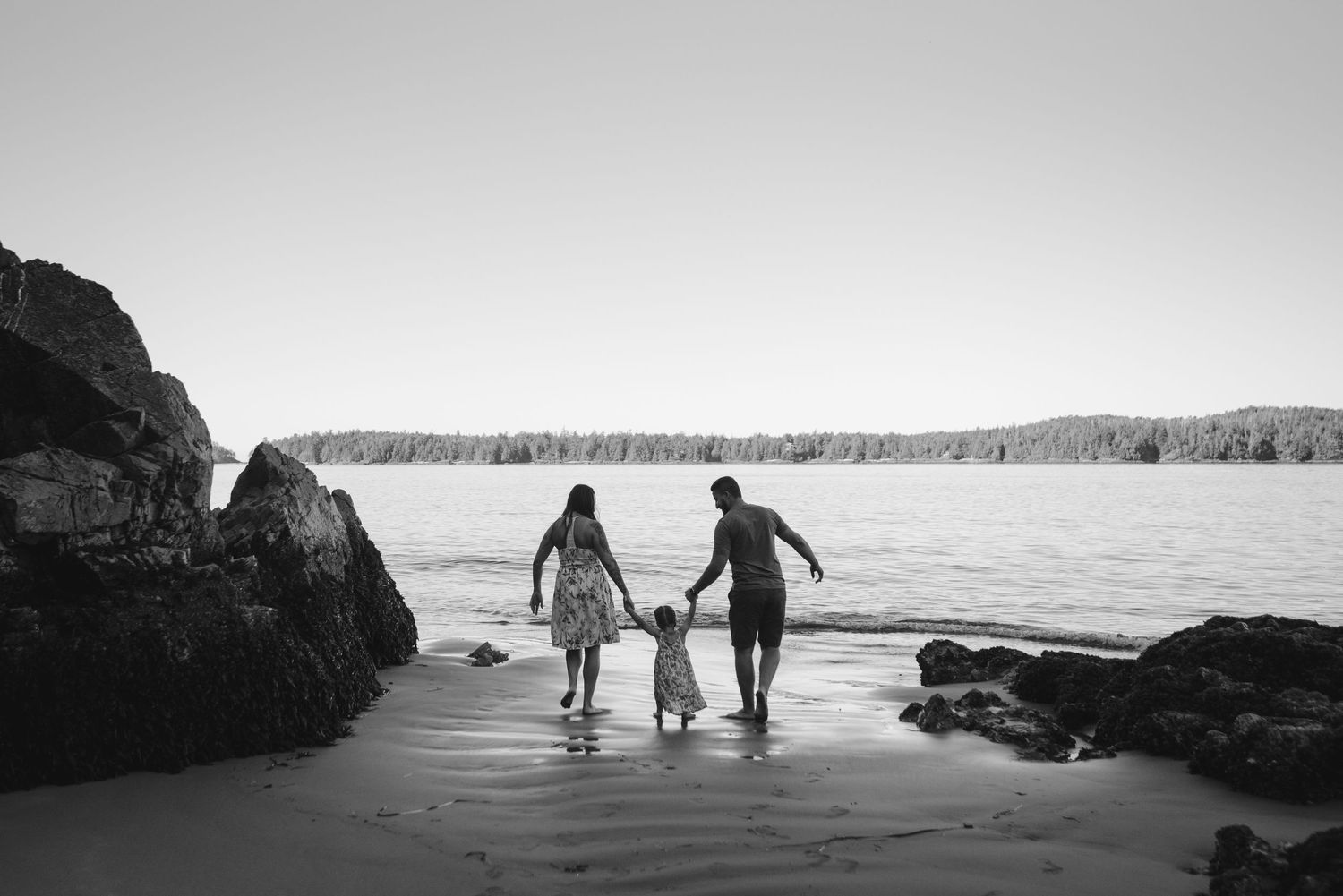 A black and white silhouette of a family walking together on a beach at sunset.