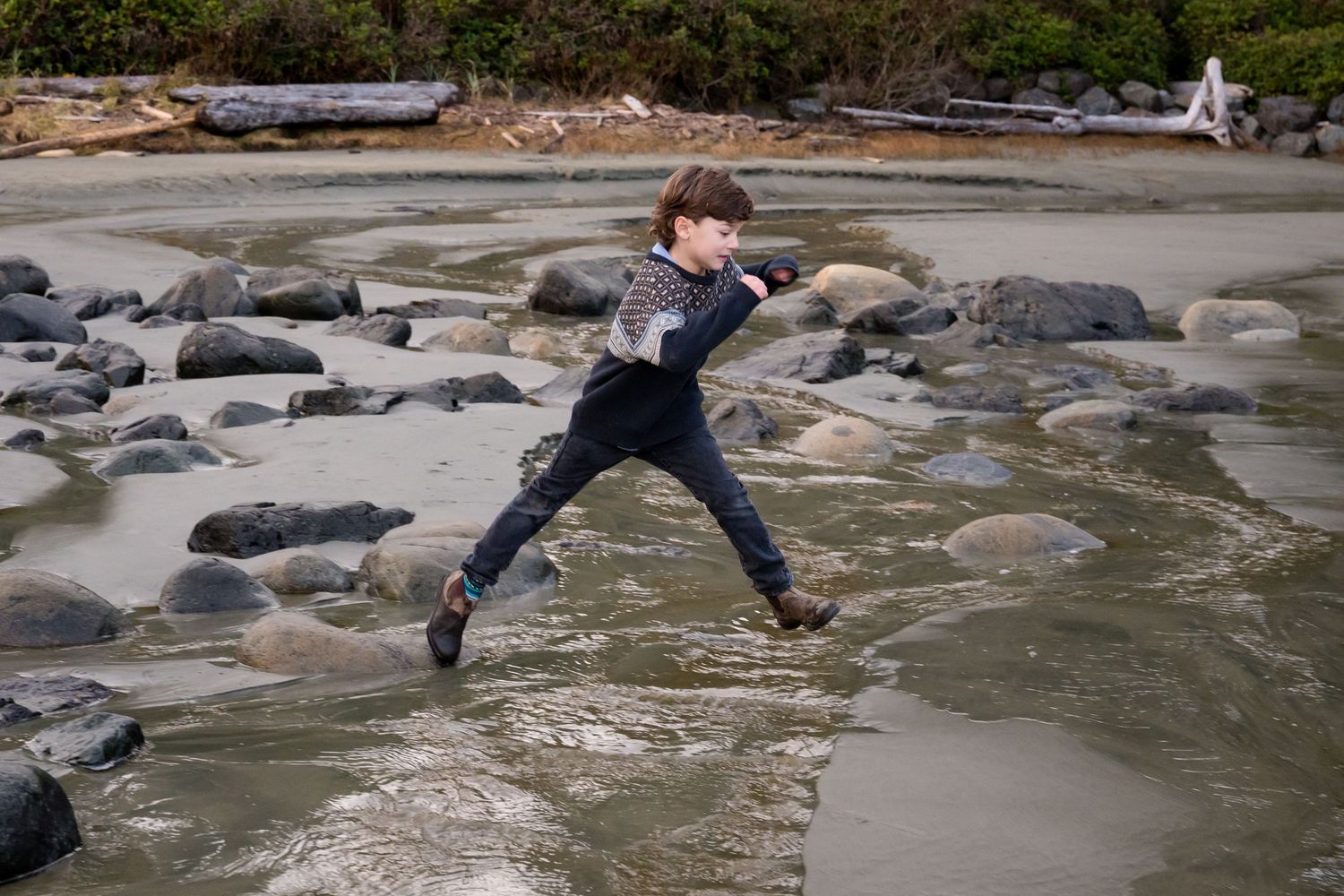 People jumping across rocks on a beach during low tide.