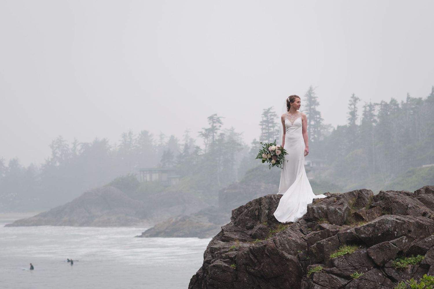A bride stands alone on a dramatic coastal cliff with misty ocean views in the background.