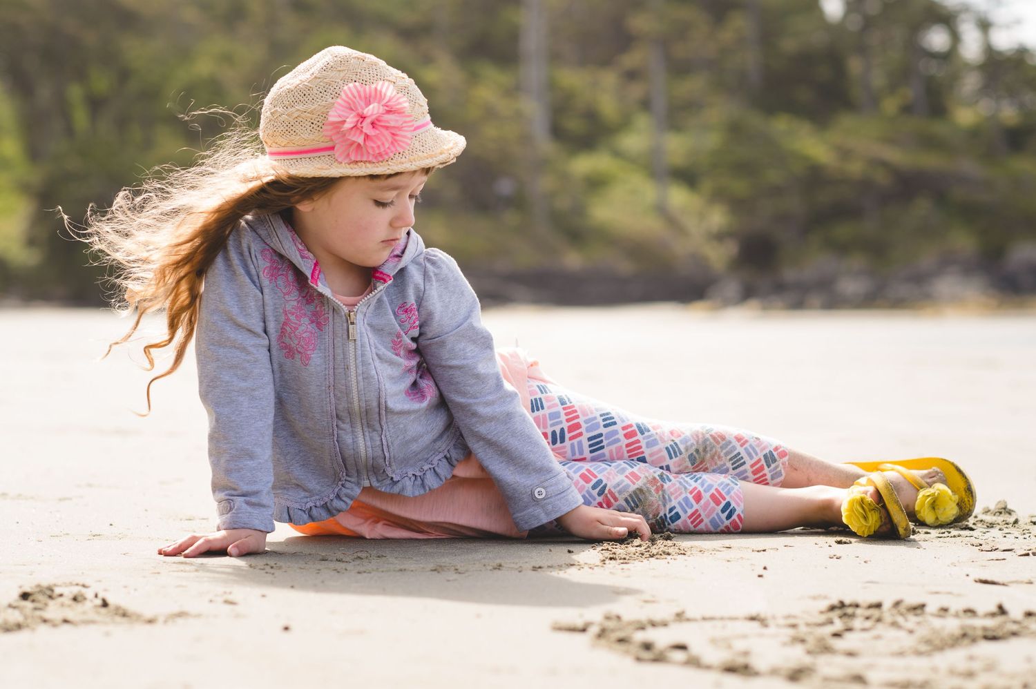 A girl lying on the beach sand wearing a pink hat and denim shirt during a casual photoshoot.