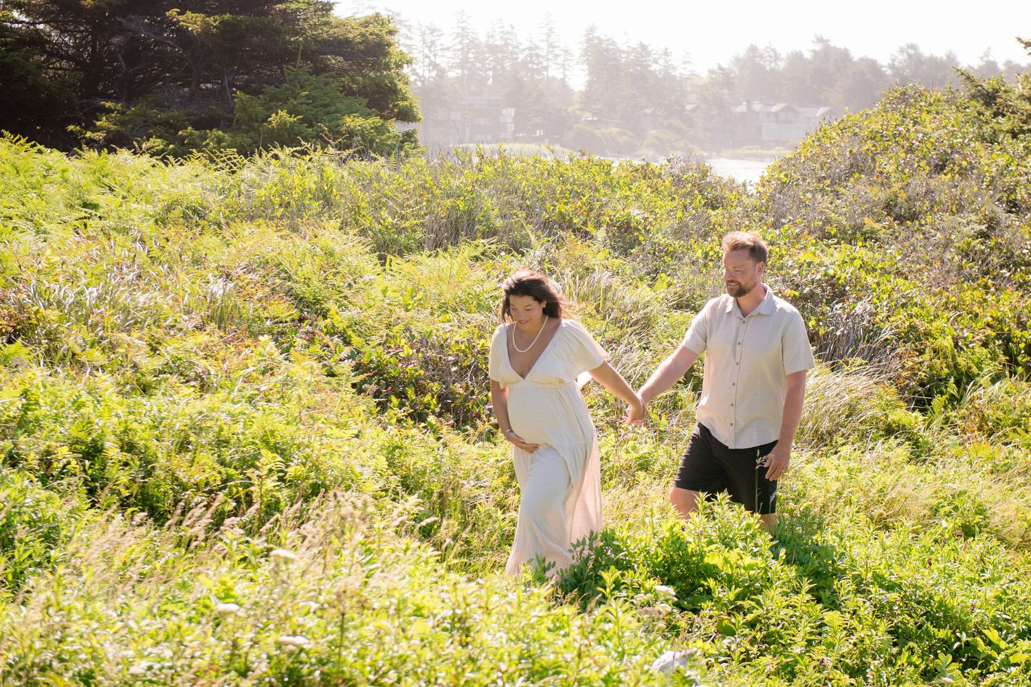 A couple walks through coastal vegetation with ocean views in the background.
