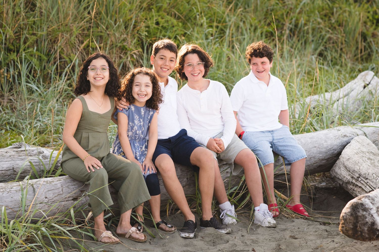 Family group seated together on coastal driftwood with beach grass backdrop.