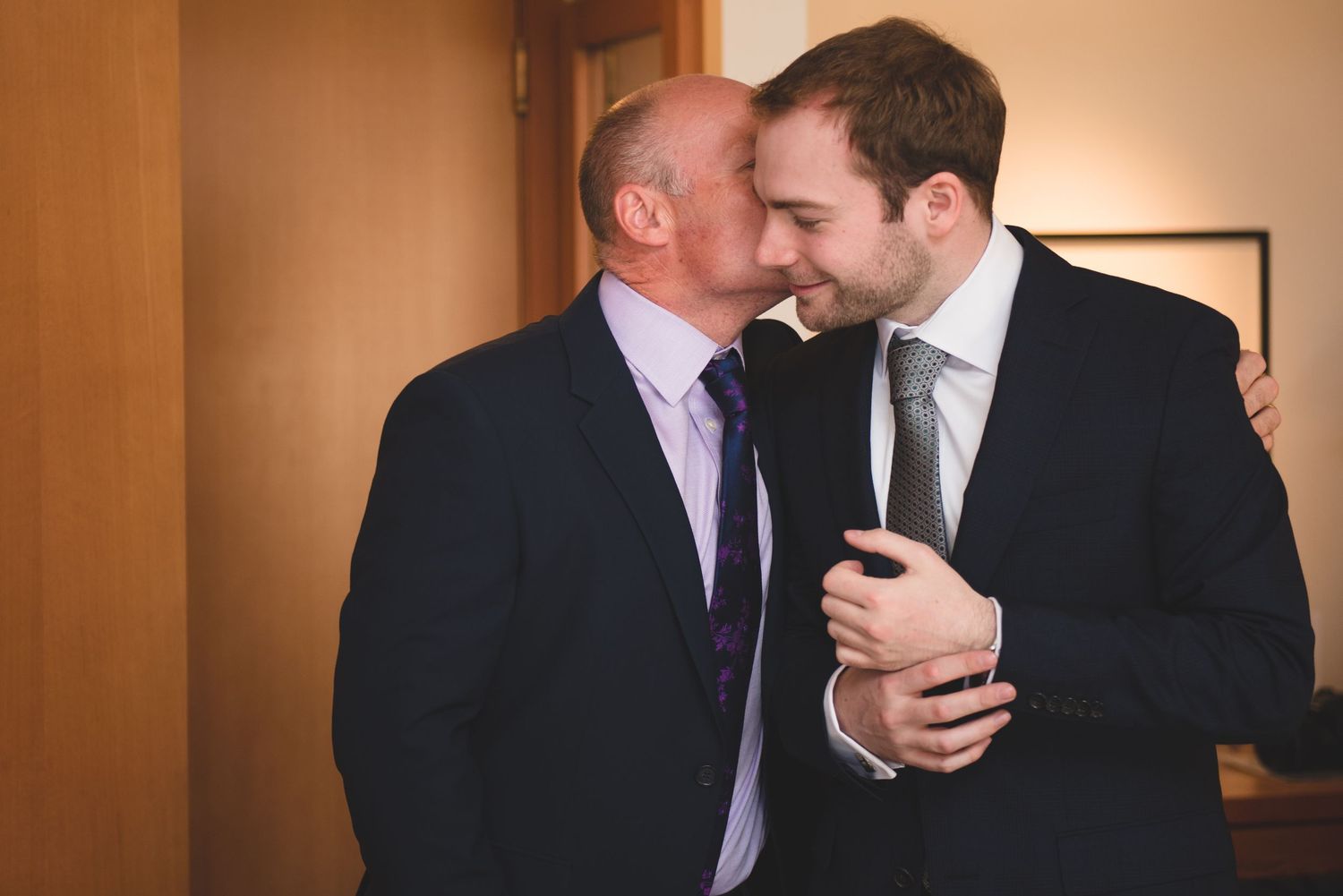 Two men in formal attire share a candid moment during wedding preparations.