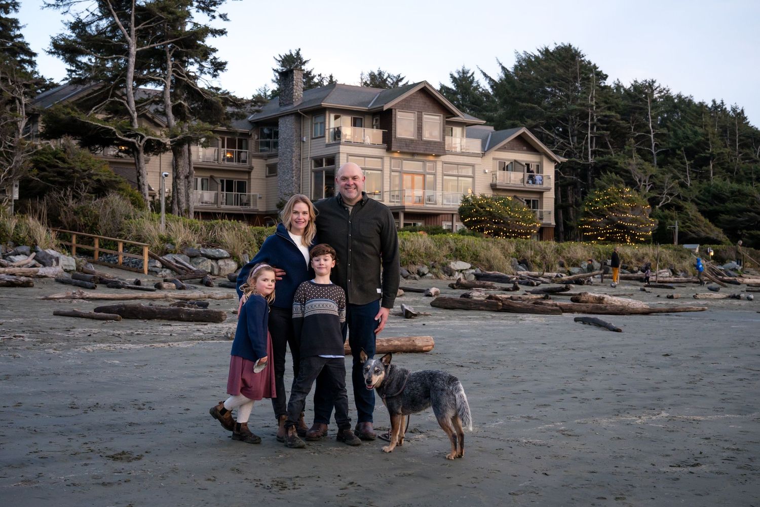 People and dog exploring rocky beach landscape near coastal homes.