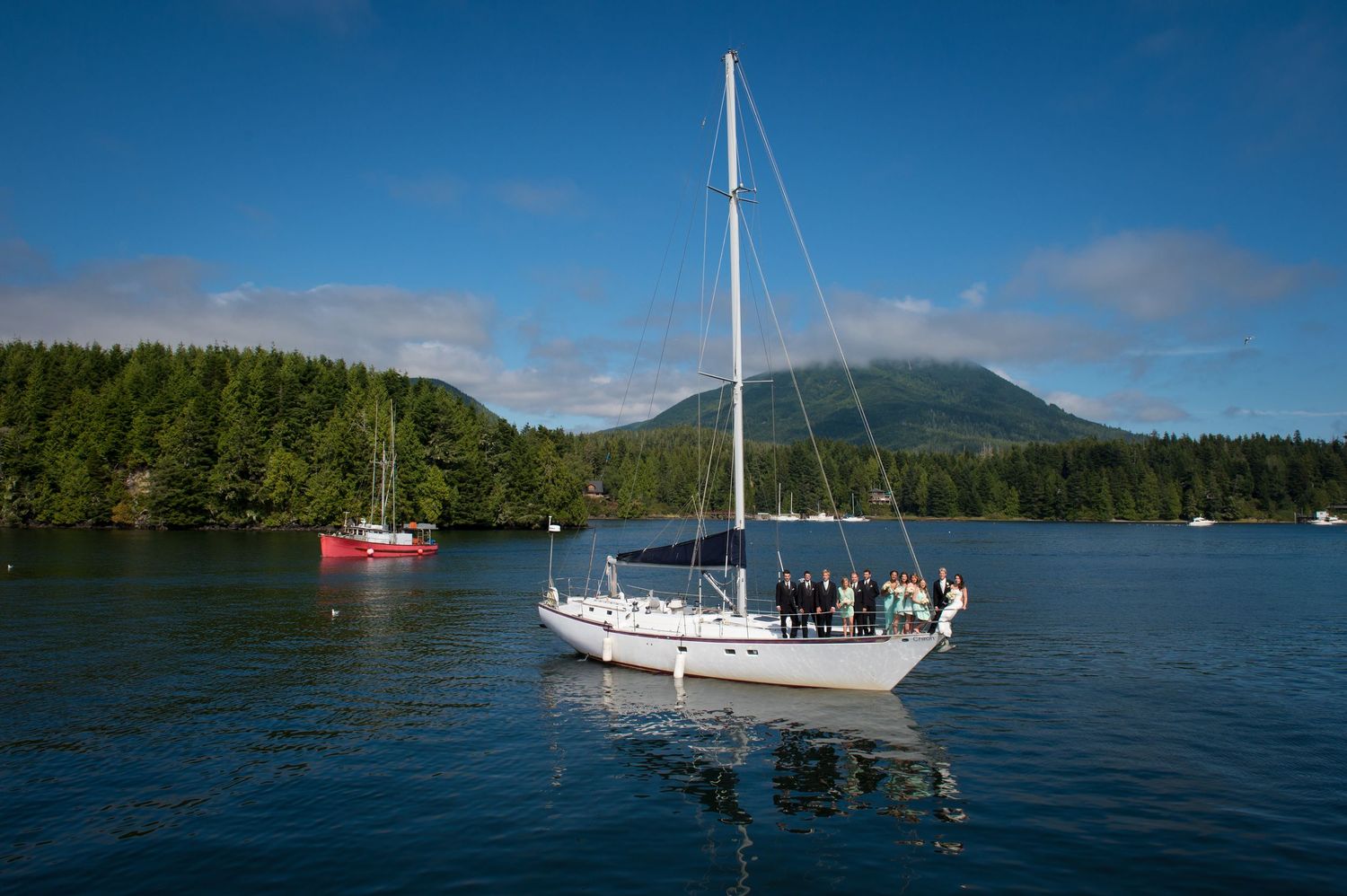 Sailboats anchored in calm waters surrounded by forested mountains and blue skies.