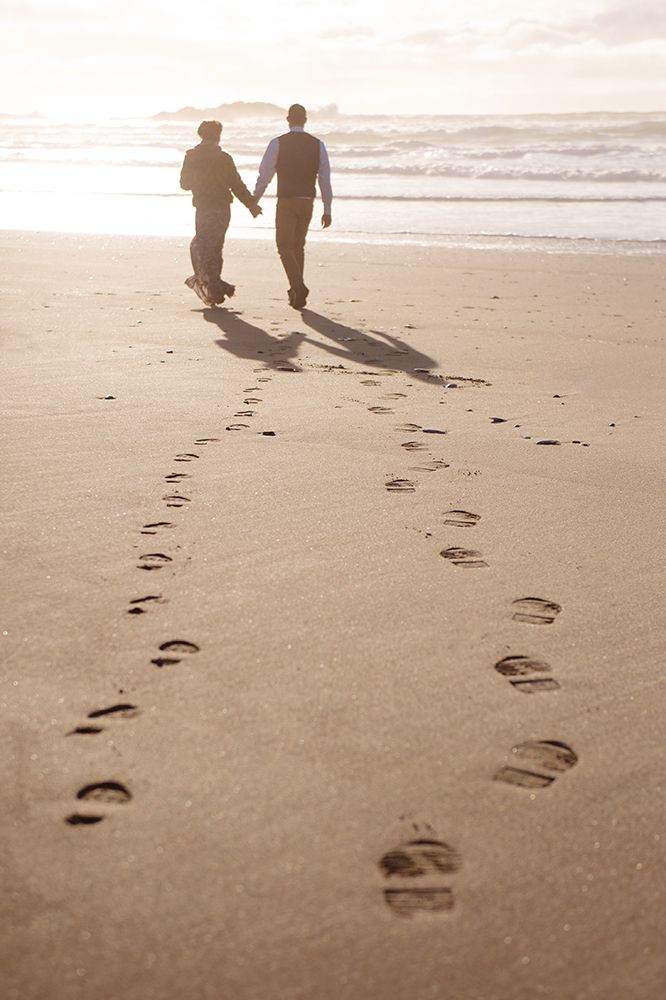 Footprints in the sand lead to a couple walking along a peaceful beach at sunset.