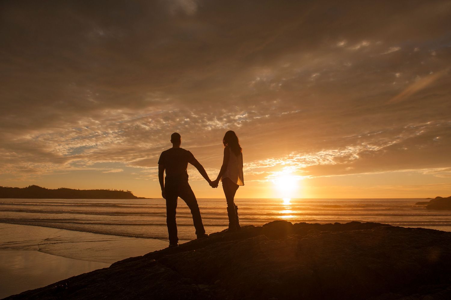 Silhouettes of people walking on beach at sunset with dramatic orange sky and ocean waves in background.
