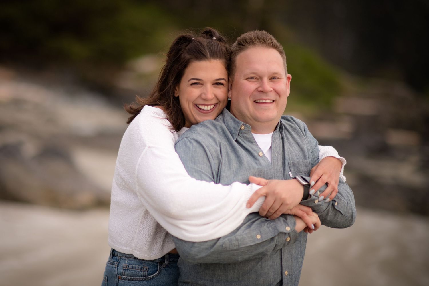 A couple embraces and laughs together on a rocky beach during a photo session.