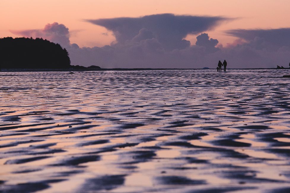 Two silhouettes stand on the horizon during a vibrant sunset over rippling ocean waters.