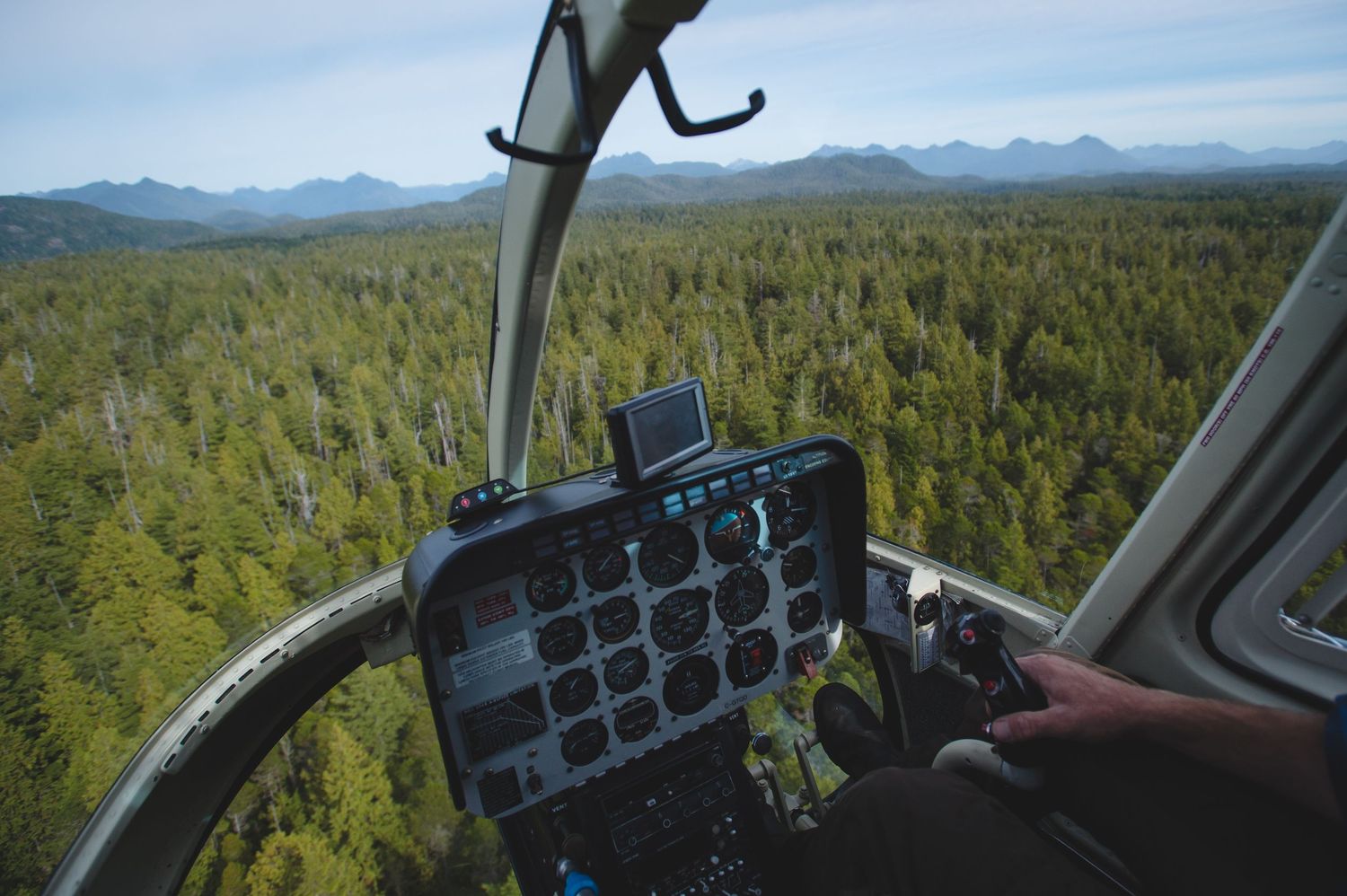Aerial view of mountains and forests stretching to the horizon from a helicopter cockpit.