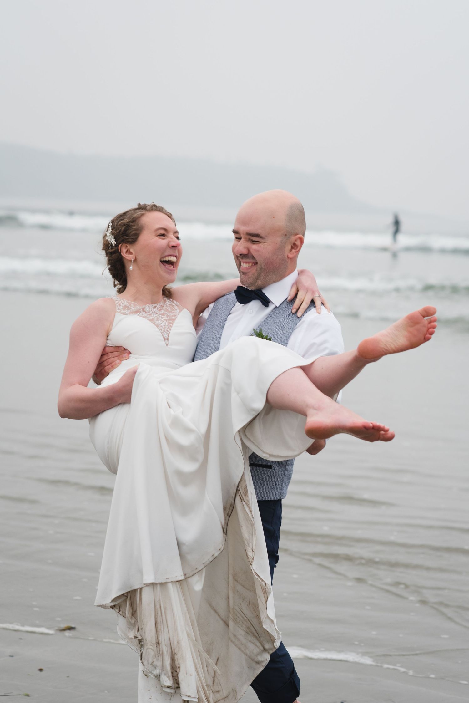 Happy couple in wedding clothes laughing and dancing together on a cloudy beach.