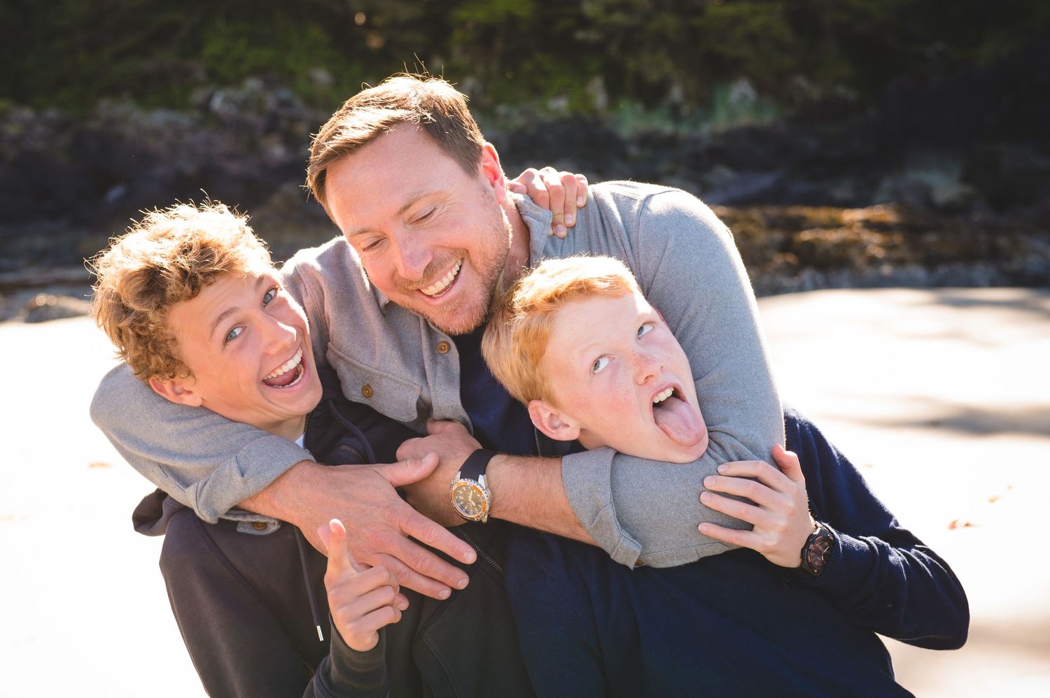 Playful family moment captured on a sunny beach with natural expressions.