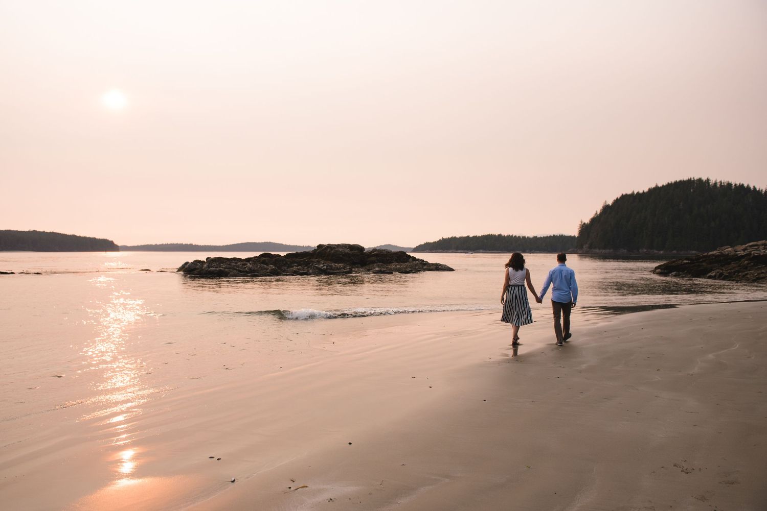 Silhouettes of people walking along a peaceful beach at sunset with golden light reflecting on the water.