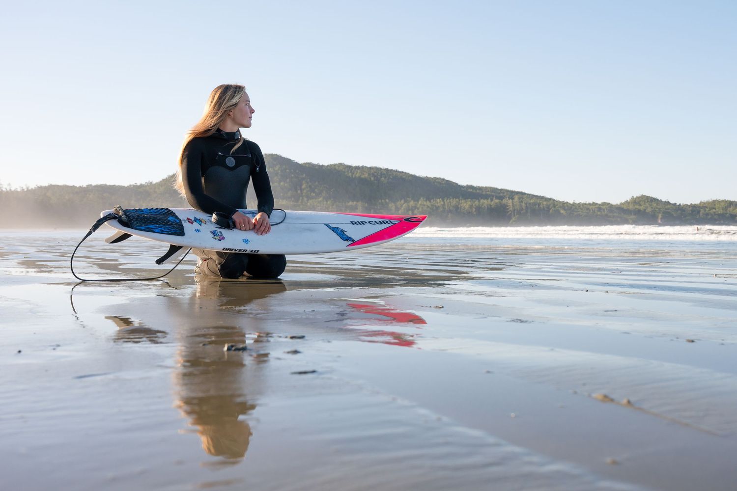 A surfer in a wetsuit performs a graceful duck dive under an approaching wave at a scenic beach.