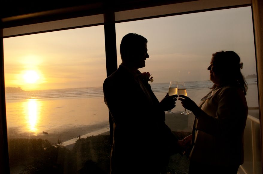 A silhouetted couple toasts with wine glasses against a golden sunset over the ocean.