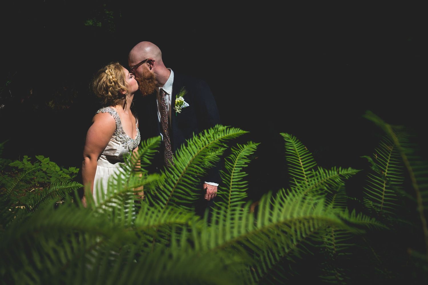 Artistic wedding photography with ferns and natural greenery in the foreground.