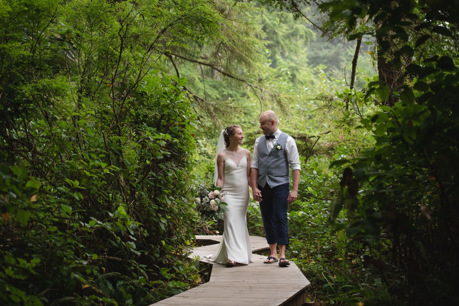 A couple walks along a scenic forest path surrounded by lush green foliage.
