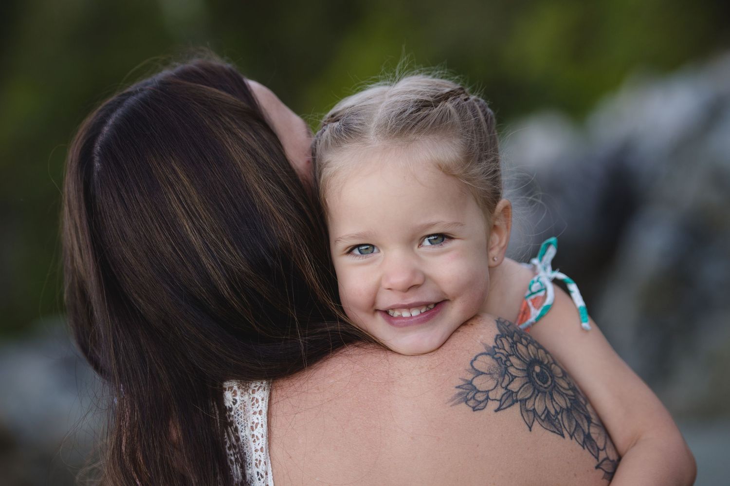 A sweet embrace captured outdoors with a visible floral tattoo and natural background.