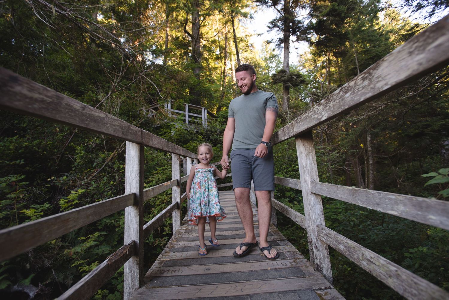 Natural family photos on rustic wooden walkway surrounded by evergreens.