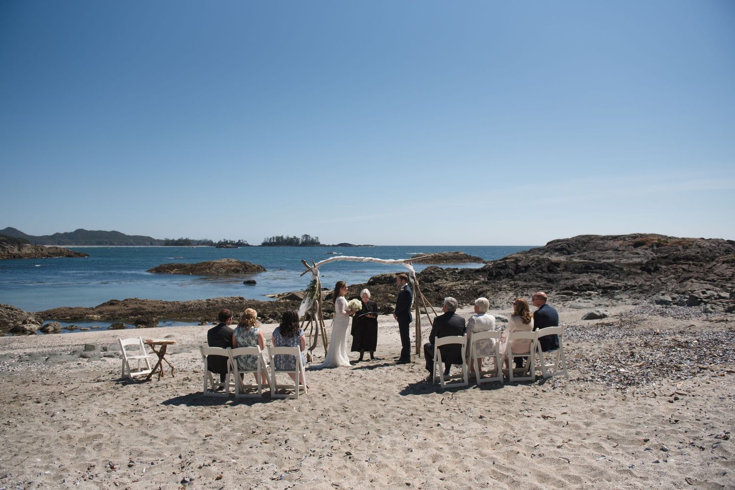 Wedding ceremony setup with white chairs on a rocky beach overlooking the ocean.