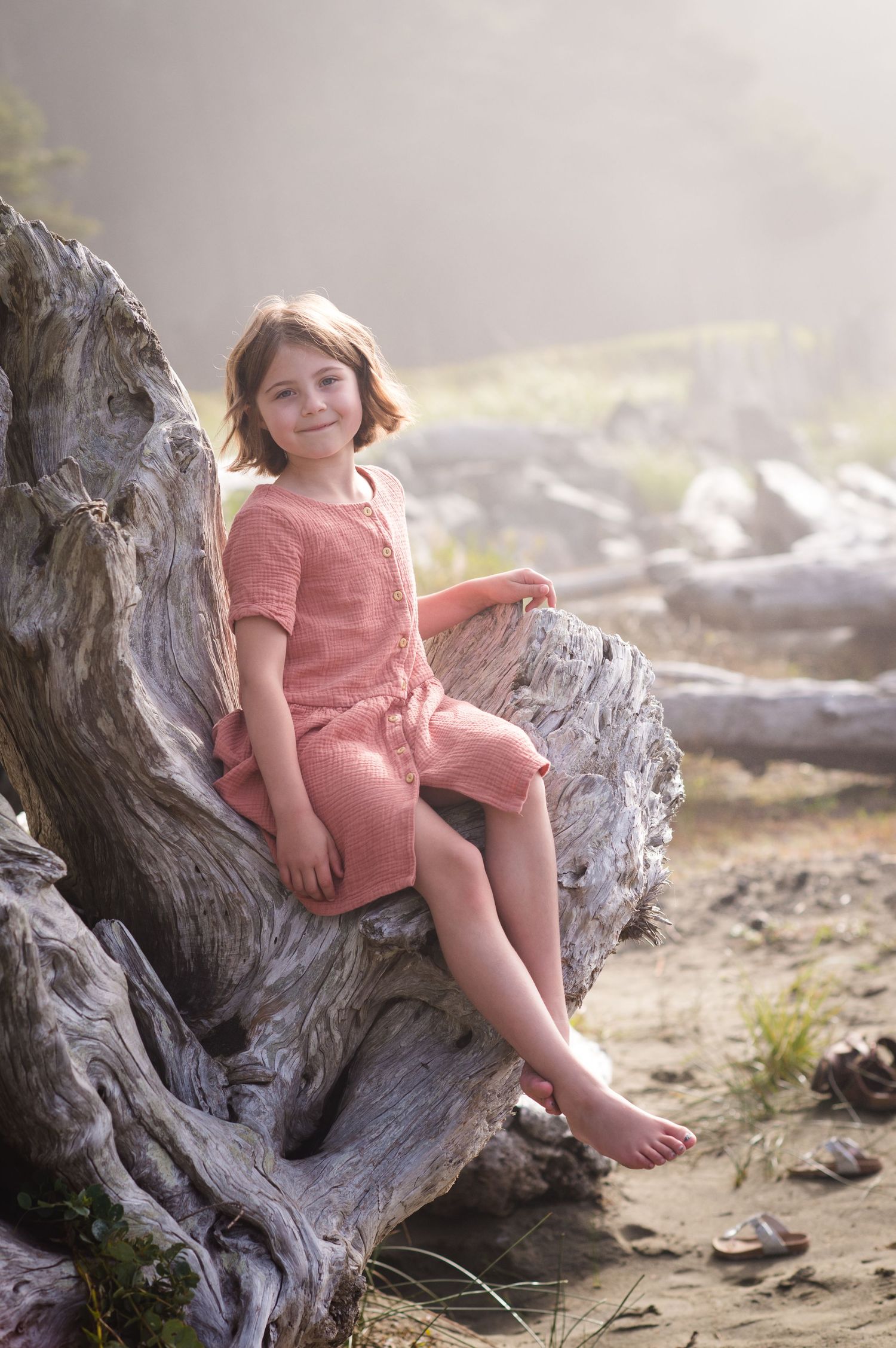 Someone in pink sits on a large piece of driftwood at the beach during golden hour.