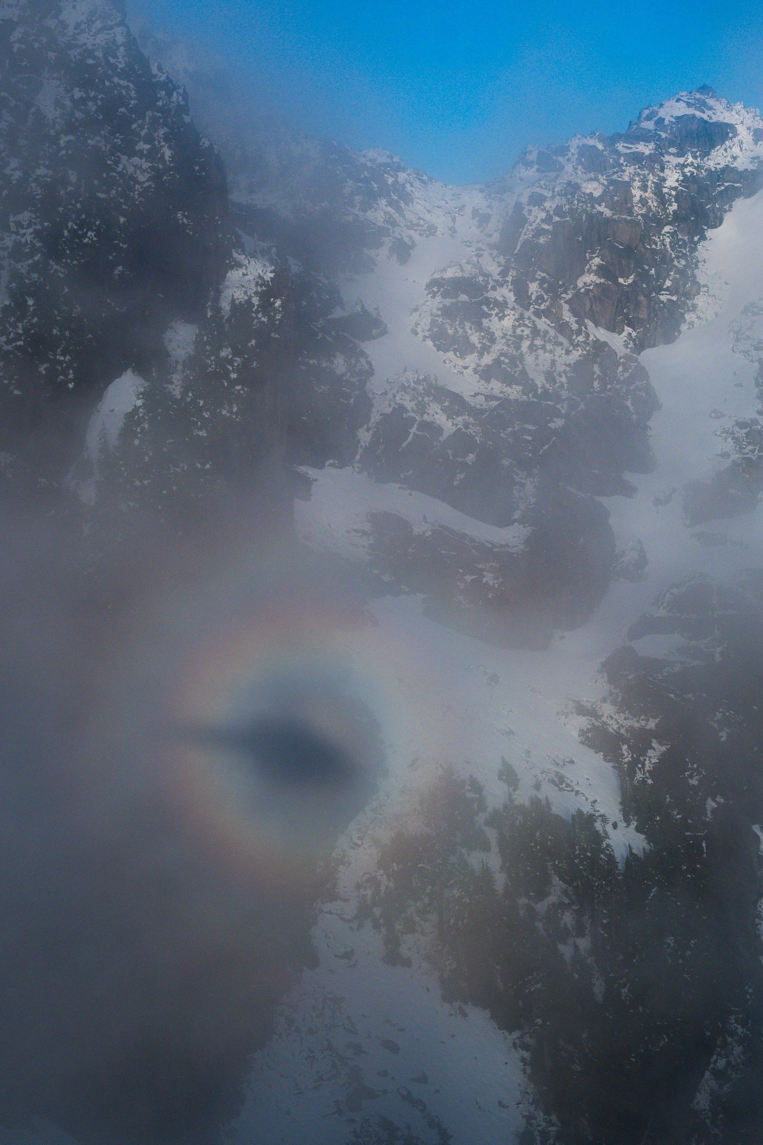 Rare circular Brocken spectre rainbow phenomenon visible through misty clouds over snowy mountain peaks.