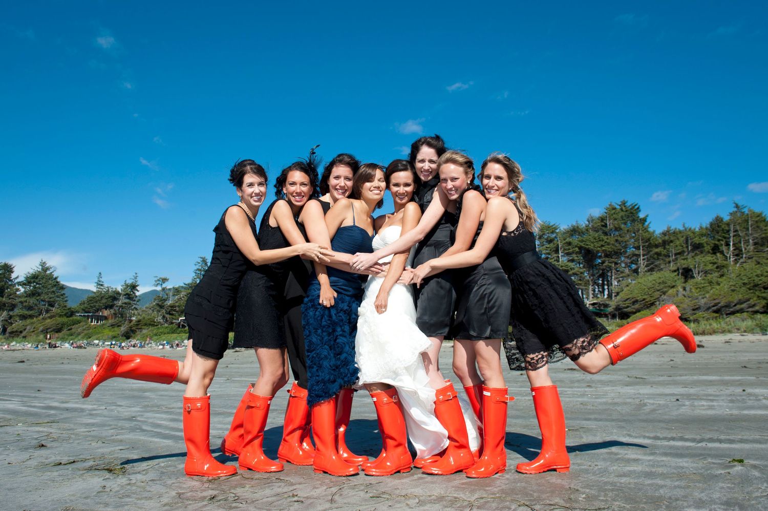 Wedding party poses playfully on beach wearing red socks against blue sky background.
